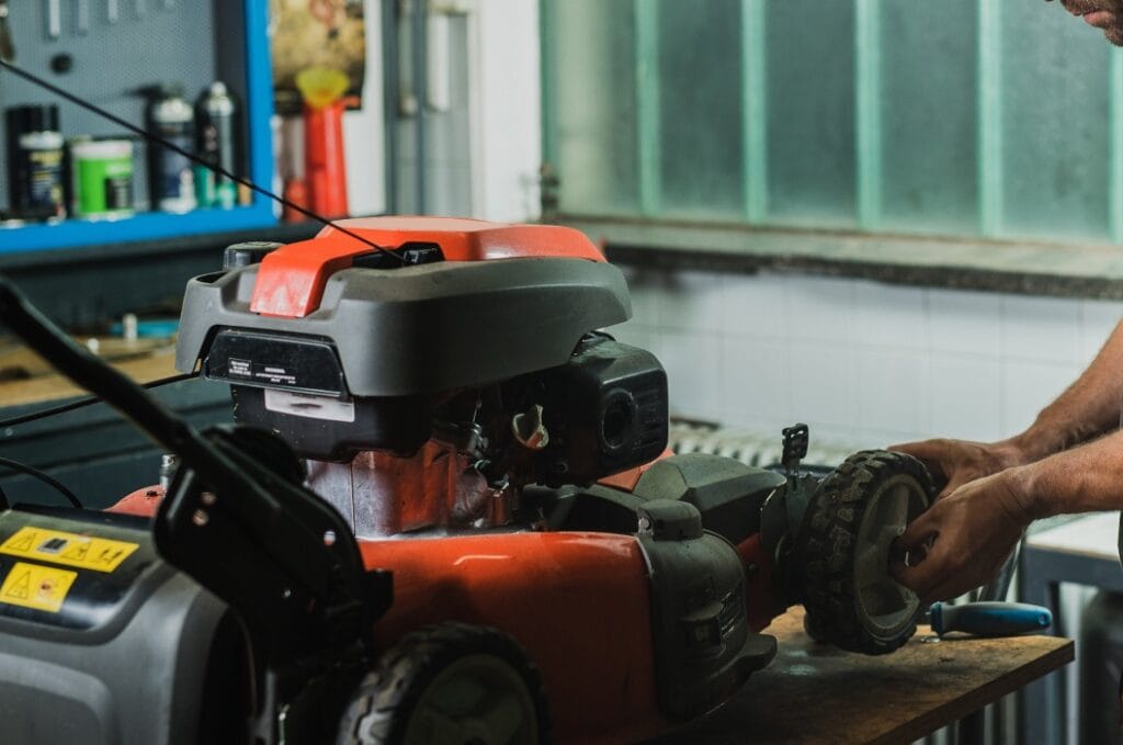 Professional serviceman is repairing a lawnmower, refitting a front wheel. Man repairing a mower in a workshop